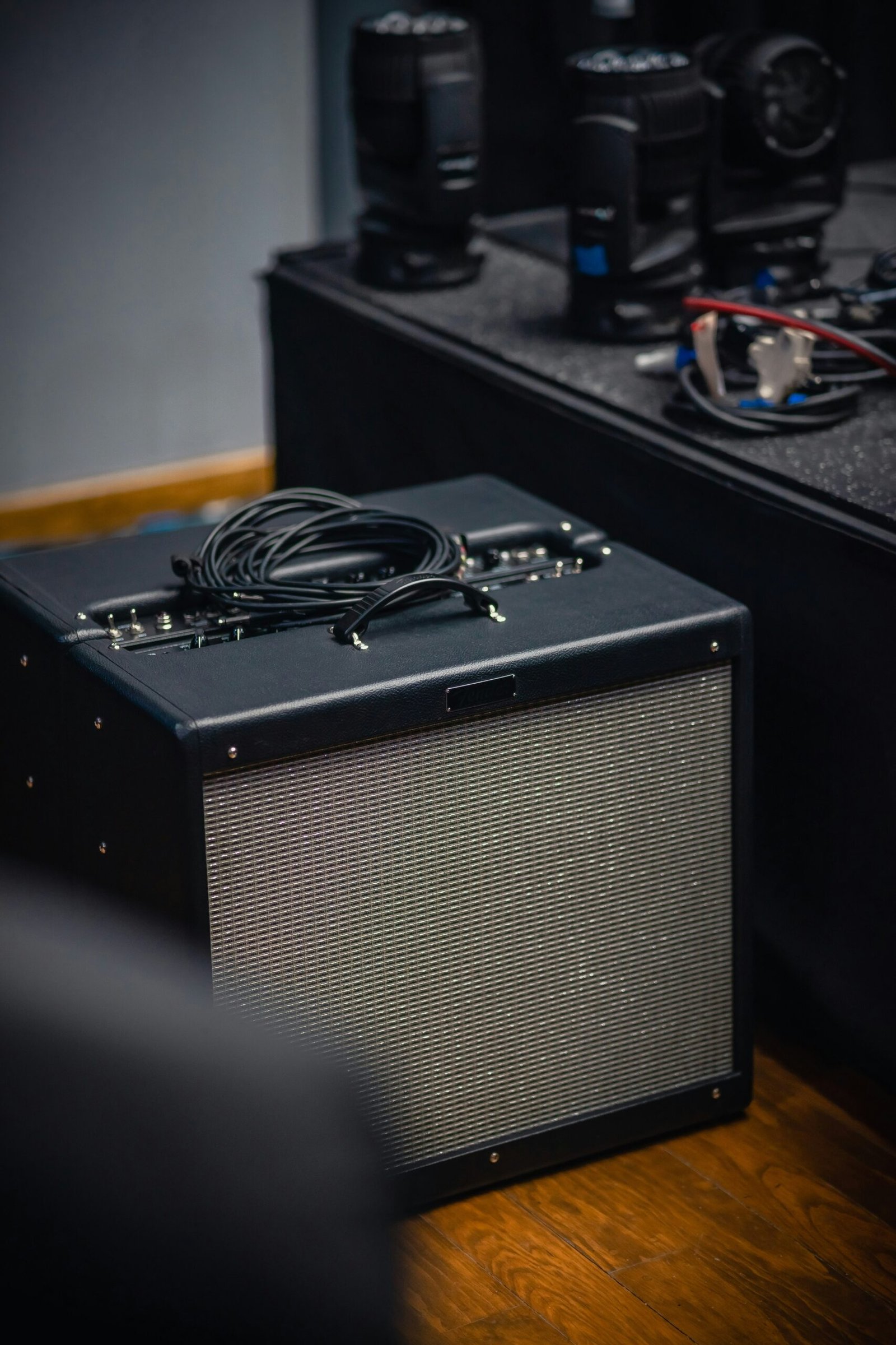 Black guitar amplifier on a wooden floor with coiled cables placed on top, surrounded by other stage equipment.